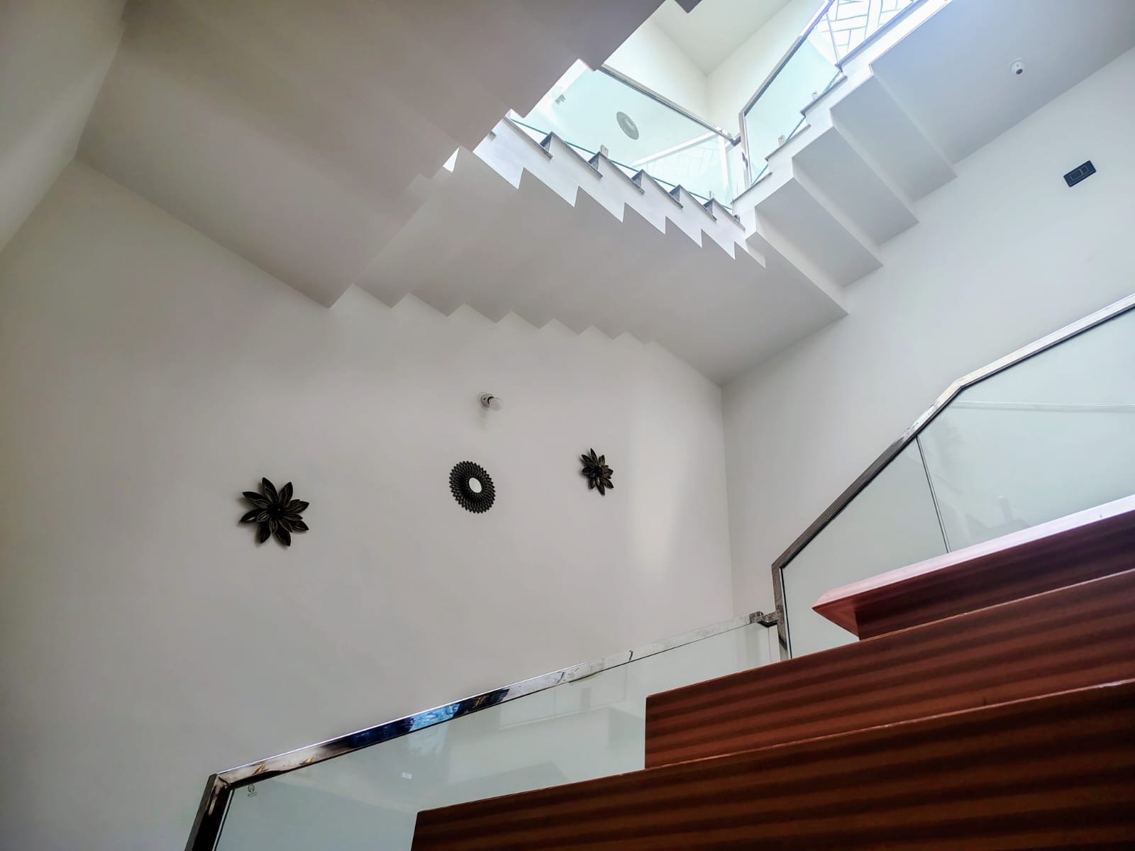 Double-height stairwell lit by an overhead skylight, with a glass and timber staircase and wall-mounted decorative discs